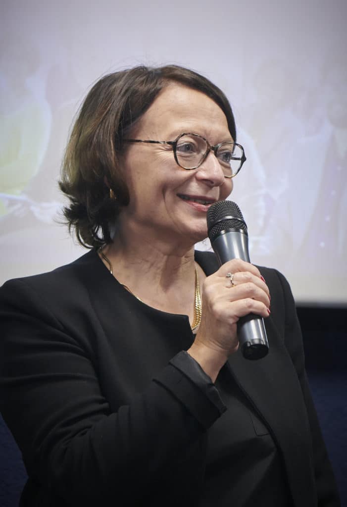 Christine huchette sur scène tenant un micro et souriante.